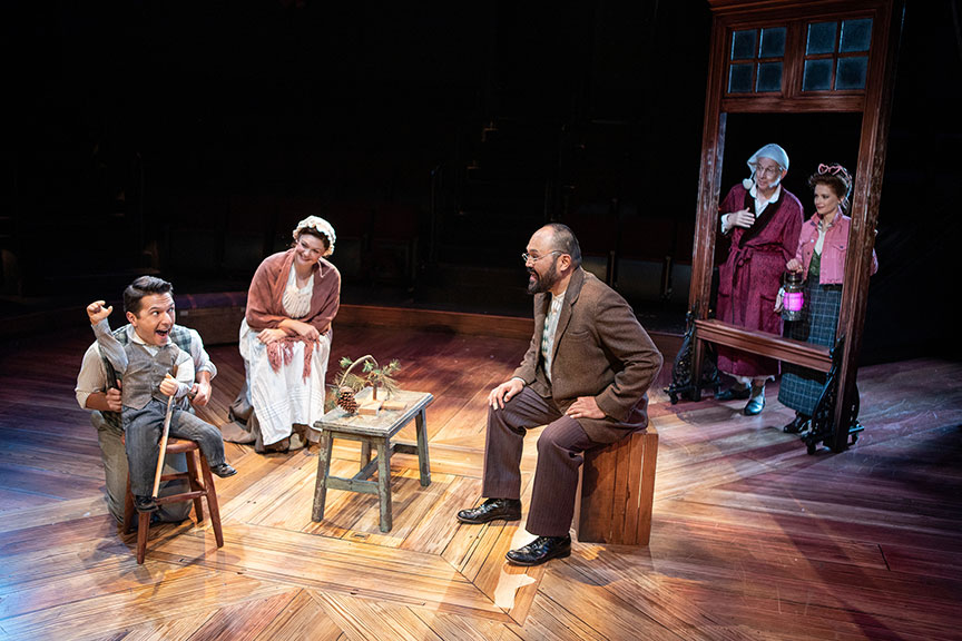 Dan Rosales as Tiny Tim, Jacque Wilke as Mrs. Cratchit, Orville Mendoza as Bob Cratchit, Robert Joy as Ebenezer Scrooge, and Cathryn Wake as Ghost of Christmas Present. Ebenezer Scrooge's BIG San Diego Christmas Show runs November 23 – December 29, 2019 at The Old Globe. Photo by Jim Cox.